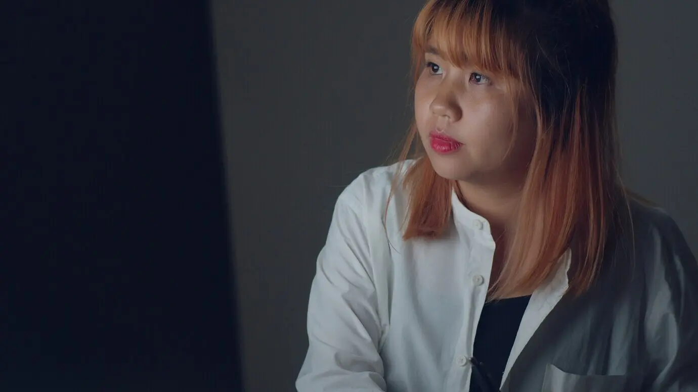 Молодая азиатская женщина допоздна работает за настольным компьютером за столом в гостиной дома.